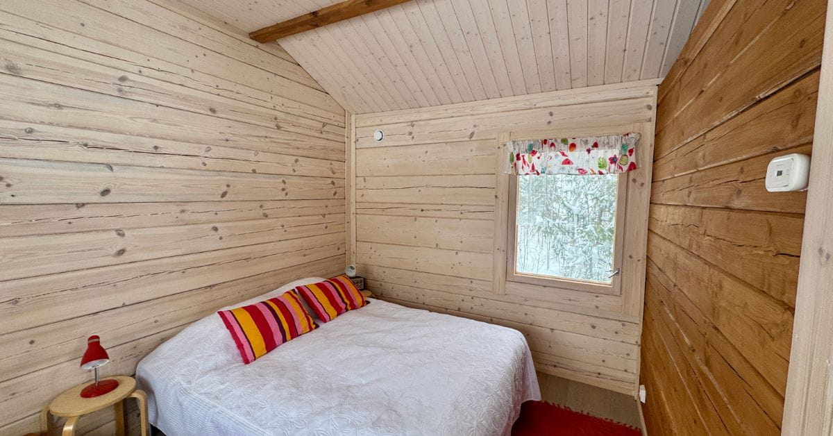 Kuvassa hirsimökin tupa, jossa näkyy sänky ja pieni ikkuna.